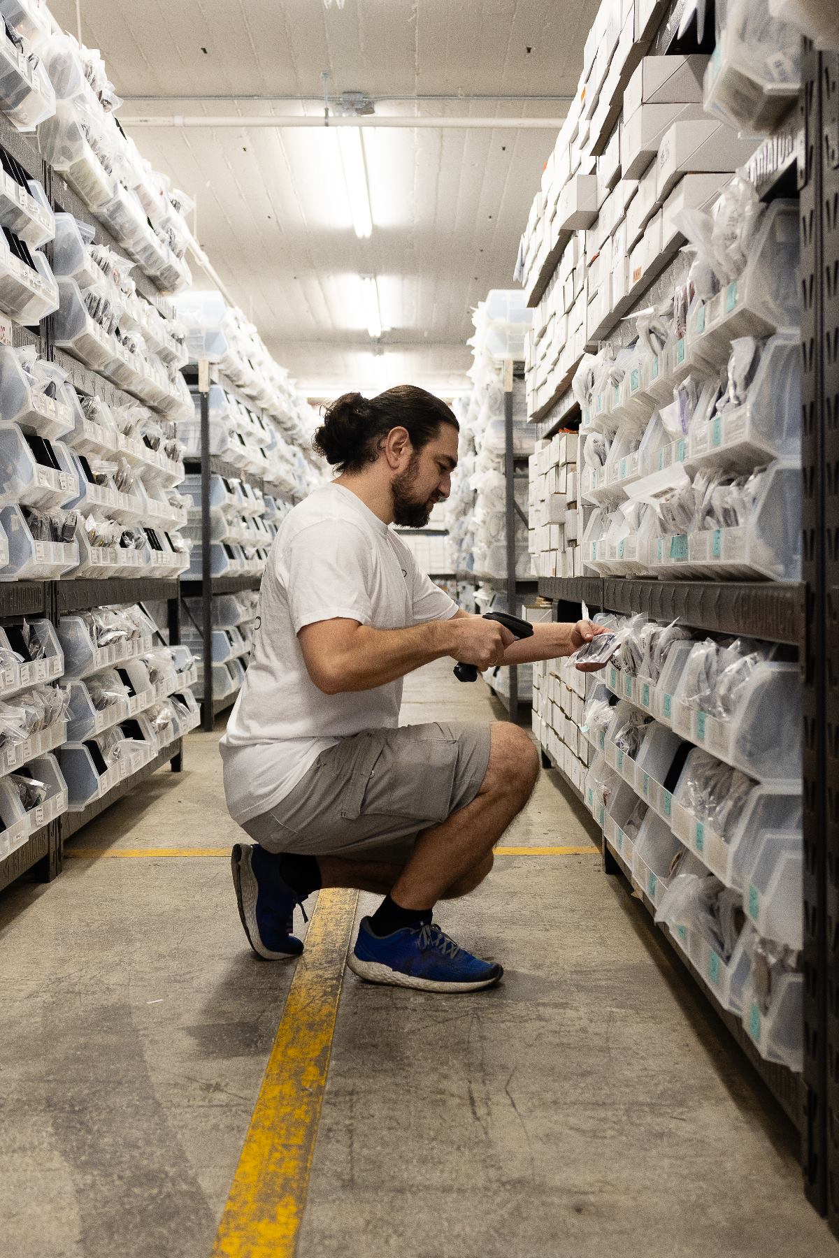 NYWD warehouse associate scanning packaged eyewear in a stocked inventory aisle in Brooklyn